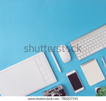 top view of office desk workspace with smartphone, notebook, graphic tablet, keyboard and mouse on blue background with copy space, graphic designer, Creative Designer concept