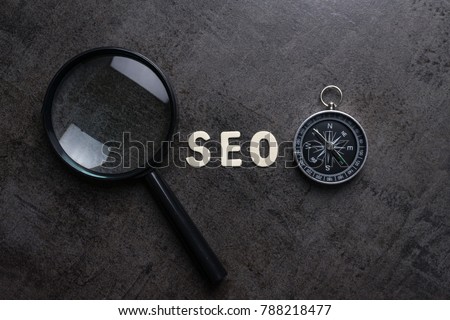Magnifying glass, alphabet SEO and compass on dark cement background using as SEO Search engine optimization concept.