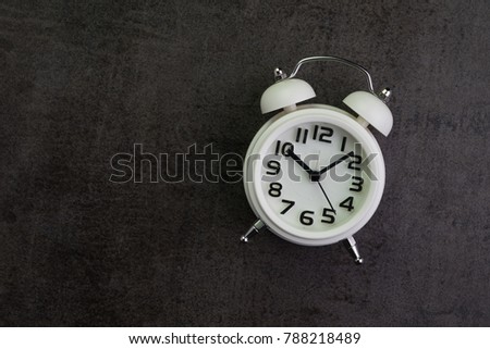 White alarm clock in retro dark black background with copy space using as time passing or alert reminder.