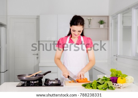 Picture of beautiful woman cutting a carrot while cooking in the kitchen