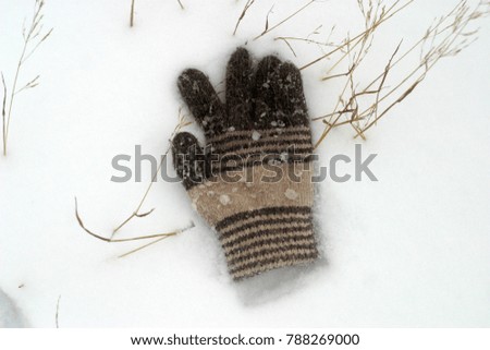 The lost children's woolen glove lies on the white snow. Winter background