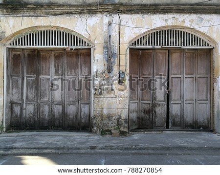 The old yellow building with wooden door. It 's cracks in the wall and it 's had black stains on the walls and doors, at Chantaboon Waterfront Community, Chanthaburi, Thailand.