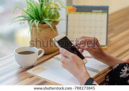 Woman holding smartphone to update calendar with notebook pencil diary vase on table with blurred calendar. planning scheduling agenda and event for 2018. Calendar and Planning concept. Royalty-Free Stock Photo #788273845