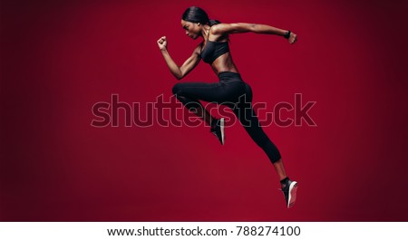 Sports woman running over red background. Full length shot of healthy young african woman sprinting.