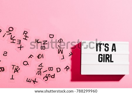 Light box with girl baby announcement text on girly pink background, surrounded by letters in chaotic order