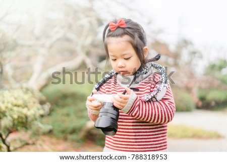 Cute little asian girl takes picture with mirrorless camera in winter in Japan garden.