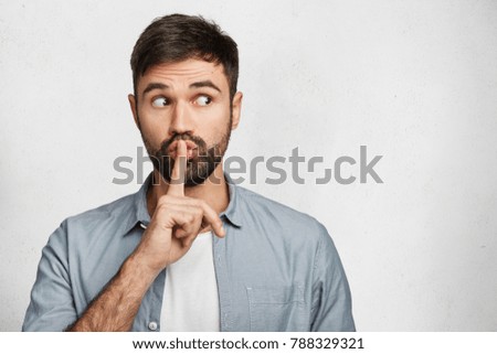 Serious good looking male with trendy hairdo, keeps fore finger on lips, tries to keep conspiracy, looks aside, says: Shh, make silence please. Isolated shot of attractive man shows silence sign Royalty-Free Stock Photo #788329321