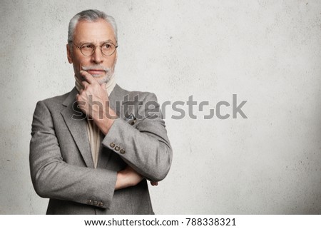 Isolated shot of handsome thoughtful businessman dressed in formal suit, looks thoughtfully aside, keeps hand under chin, tries to generate new ideas for startup, isolated on white wall, copy space Royalty-Free Stock Photo #788338321