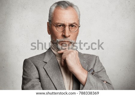 Portrait of handsome mature bearded male manager looks with strict expression directly into camera, listens to explanations from colleagues why they are late, being displeased with something Royalty-Free Stock Photo #788338369
