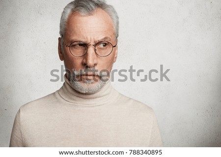 Thoughtful grandfather has grey hair, mustache and beard, dressed casually, looks aside through spectacles, being deep in thoughts, analyzes his actions and different life situations isolated on white Royalty-Free Stock Photo #788340895