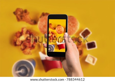 Female hands taking photo of tasty burger with snacks on table