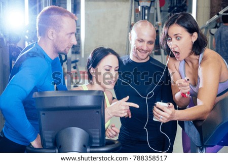 cheerful friends in the gym have fun and watch videos on the phone