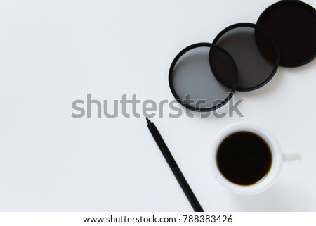 Top view of photography work desk. Flat lay workspace with photographic filters, cup of coffee and pen on white background. Minimal, black and white tones and space for text