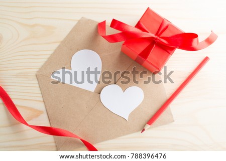 Letter with heart-shaped Valentine's day greeting card and red present box on wooden table.