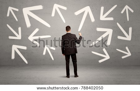 An elegant businessman standing with his back in front of urban wall full of arrows pointing in different directions concept