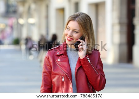 Front view portrait of a fashion blonde calling on phone and looking at side walking towards camera on the street