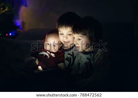 Three brothers, sitting at home on sofa in living room, reading a book at Christmas, fairy tale, magic picture 