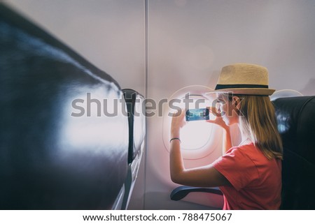 Travel and technology. Young woman in plane taking photo on her smartphone while sitting in airplane seat.
