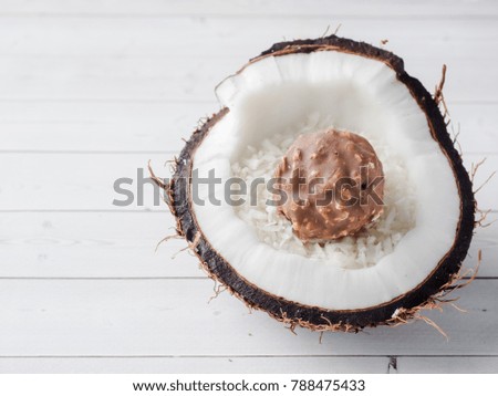 Half of the fresh organic coconut with Coconut and chocolate candy inside on wooden background.