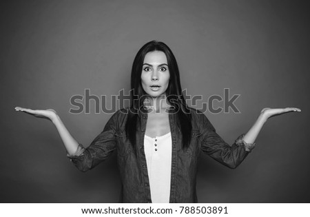 An agitated young woman in a denim shirt wondered what kind of goods she chose on a gray background isolated. Black and white photo