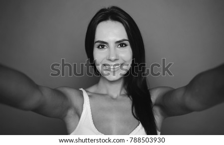 Beautiful smiling young woman photographes herself on the phone or doing selfie on a gray background isolated. Black and white photo