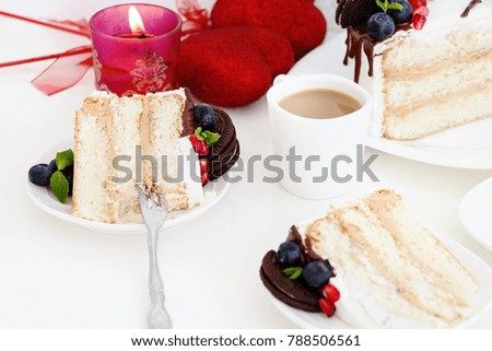 Piece of layer cake with fresh berries, cream cheese and chocolate biscuits. On white background with heart and candle. Romantic Valentine's Day concept.