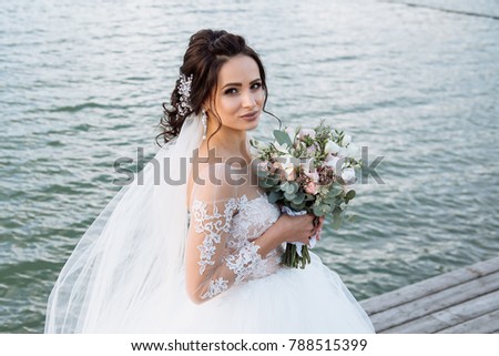 Very beautiful, dark-haired bride with ornaments in her hair, with earrings with precious stones and lush white lace dress on your wedding day.