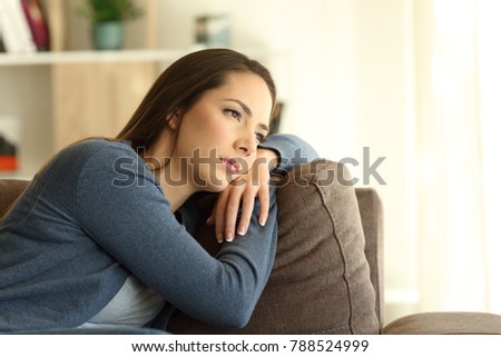 Sad woman looking trough a window sitting on a couch in the living room at home Royalty-Free Stock Photo #788524999
