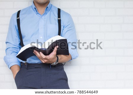 Half-length,Close up Man in blue shirt holding black book of the Bible, Buddhist, Catholic, Christian, prayer,on wall background,Copy space for your text.