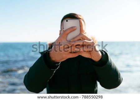 Young man taking a selfie against the background of the sea, on grey smartphone.