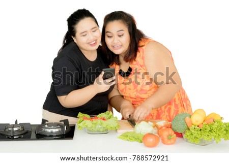 Picture of two obese women using a mobile phone while cooking together in the studio