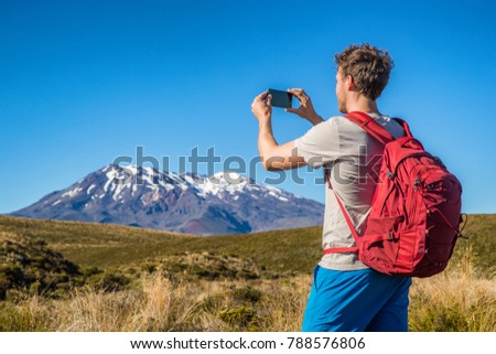 Tourist hiker man taking picture with phone of mountains in New Zealand during hike on Tongariro Alpine crossing track in New Zealand, NZ. Travel tramping lifestyle.
