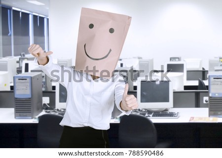 Unknown businesswoman with paper bag on her head while showing thumbs up in the workplace