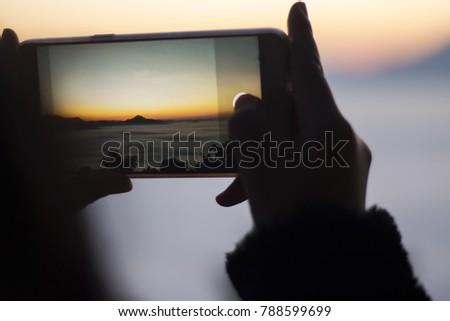 Close up woman holding a phone is taking a picture of a mountain in the morning.
