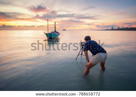 Photographer is taking a picture of sunrise with traditional fishing boats during sunset time at thailand