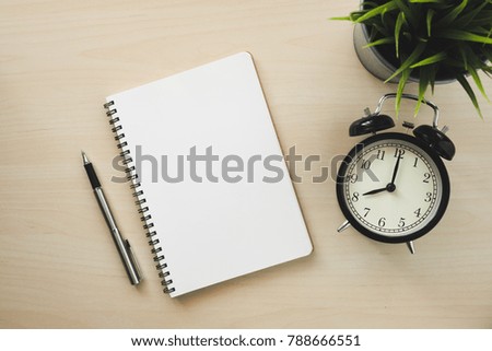 Empty white notebook top view with black alarm clock and pen on wooden table