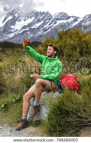 New Zealand kiwi tramper taking selfie phone picture during hike on Hooker Valley track trail in Mt Cook. Summer hiker eating lunch break during hiking. Happy man taking photos.