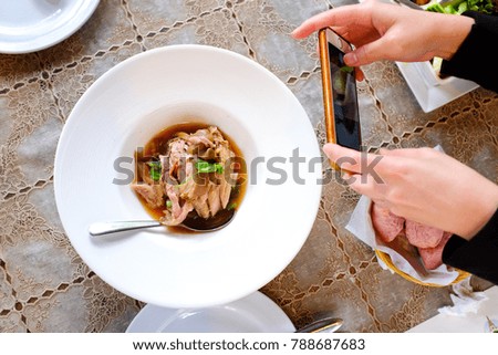 hands holding mobile phone taking photo of stewed pork served on white plate.