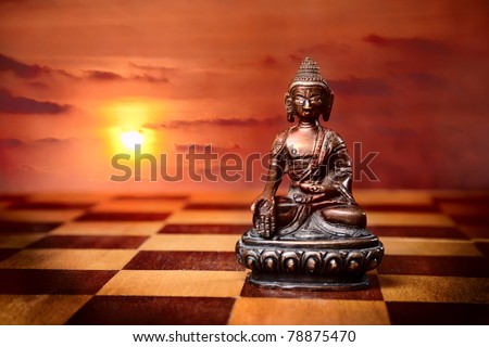 Bronze Buddha sitting in padmasana on textural chess desk floor at sunset background