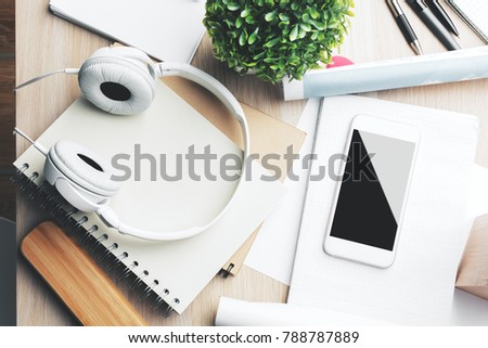 Top view and close up of creative wooden office desktop with empty smartphone, supplies, headphones and other items. Leisure, hobby, break, work and occupation concept. Mock up