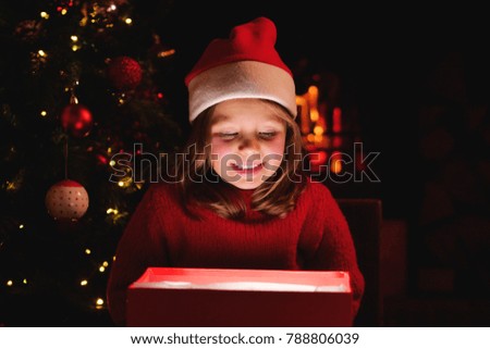 On Christmas days a little girl opens her gift under the Christmas tree, and as she opens the gift she lights up like magic. Concept of: magic, christmas, gift, holidays, happiness, love.
