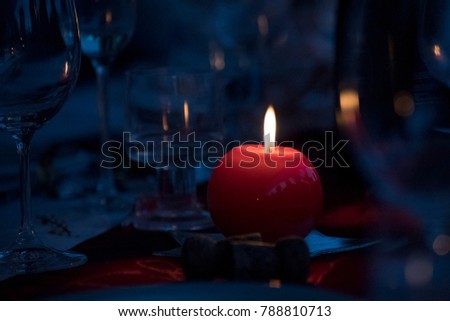 Red candle over a dinner table giving a warm, quiet, romantic and relaxing atmosphere. Dark picture with empty space for designing.