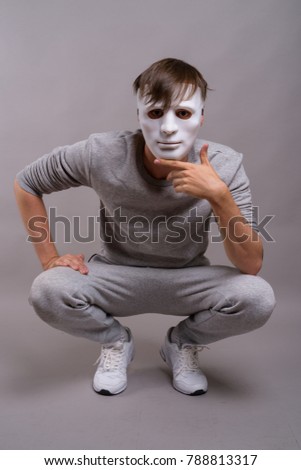Studio shot of young man wearing white mask while crouching against gray background