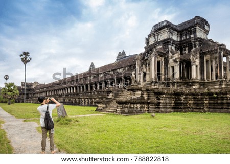 Young male tourist with smartphone taking picture of the Angkor wat under blue sky in Siem Reap, Cambodia.