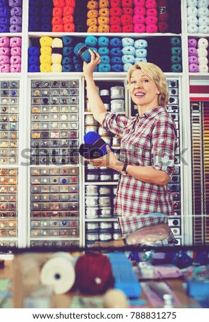 Woman seller picking yarn and wool balls for customers in local sewing store