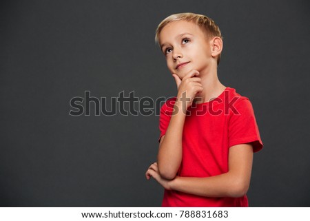 Image of thoughtful cute little boy child standing isolated over grey background. Looking aside.