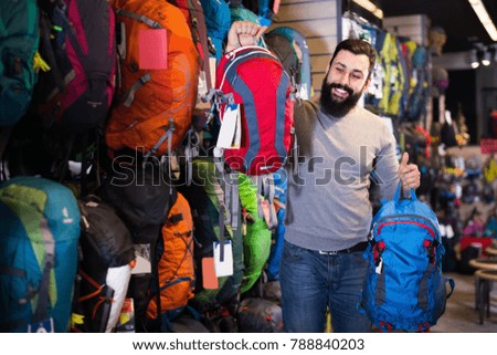 Young male customer examining backpacks in sports equipment store