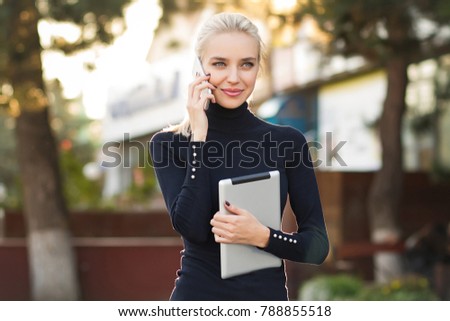 Beautiful business woman uses a tablet and speaks by phone . Student using tablet and speaks by phone in the outdoor .  Royalty-Free Stock Photo #788855518