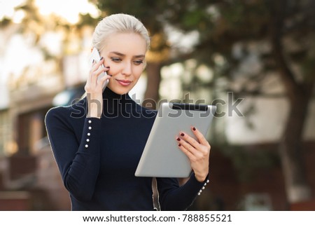 Beautiful business woman uses a tablet and speaks by phone . Student using tablet and speaks by phone in the outdoor .  Royalty-Free Stock Photo #788855521