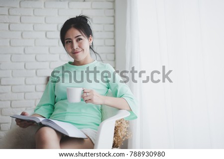Lifestyle scene of young Asian woman drinking coffee while reading book in morning time. Weekend activity and hobby concept with photo filter effect